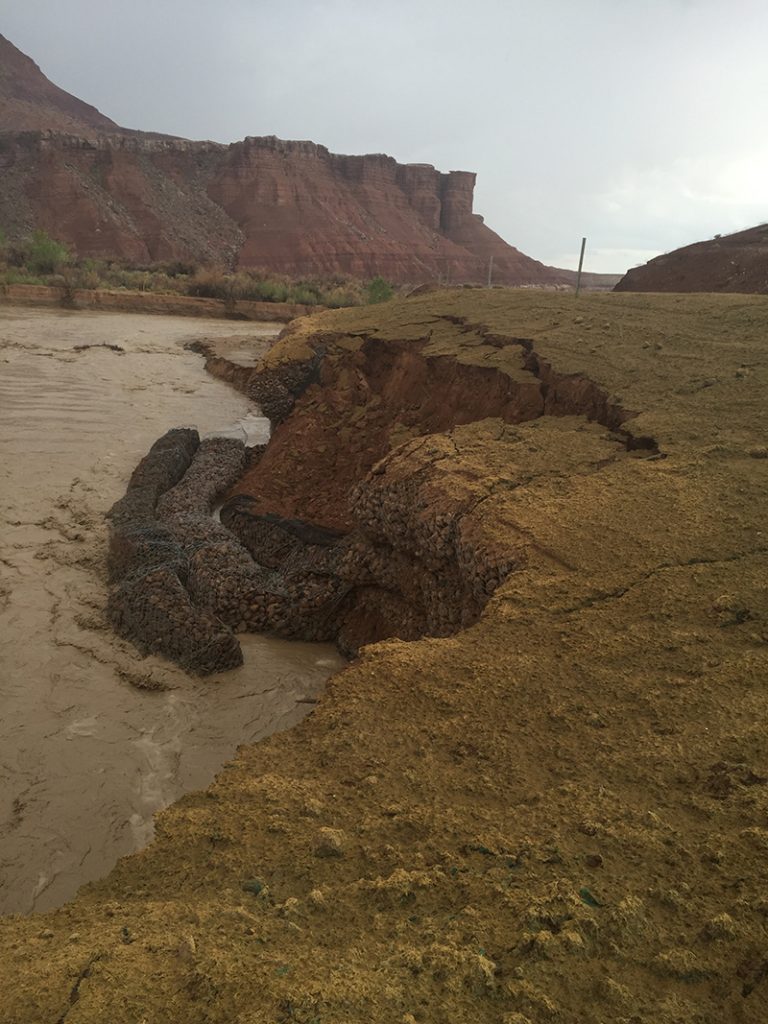 Dark sediment filled river bend with the bank falling into the water. High-flowing waters of the Paria River undercut structures intended to stabilize the riverbank along the Lonely Dell Access Road in Lees Ferry. NPS Photo
