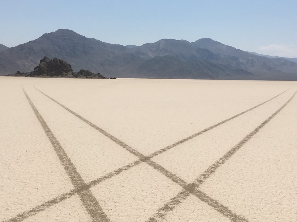 Vehicle tracks on the north end of Racetrack Playa. The Grandstand is the rock formation visible in the background. NPS Photo